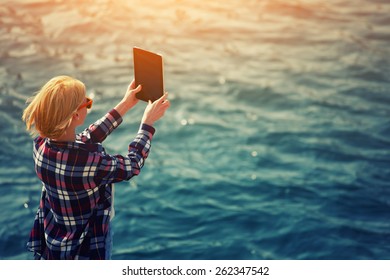 Back View Of A Woman Taking Picture With A Digital Tablet Camera Standing Against Sea Background On The Beach, Female Tourist Standing On Coastline Photographing Nature View, Flare Sun Light, Filter