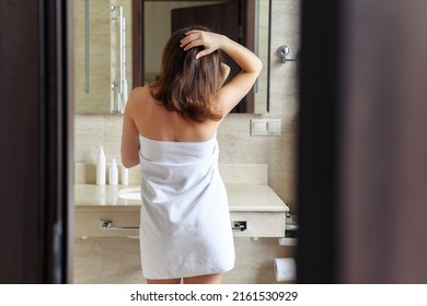 Back view of woman in a towel standing and looking in front of the mirror in the bathroom