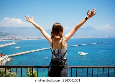 Back view of woman traveler holding hands up watching the sea from a view point in Turkey on a summer day