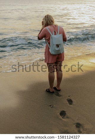 Back view of a woman walking on beautiful sea beach. Girl take the pictures with smartphone