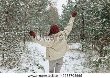 Back view of woman in warm winter clothes enjoying freedom while walking in snowy forest in cold weather 