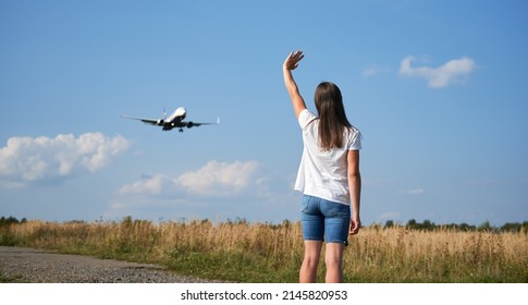 Back View Of Woman Waving Hand To Flying Commercial Airplane In The Sky. Lifestyle And Travel Concept.