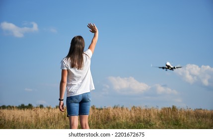 Back View Of Woman Waving Hand To Landing Commercial Airplane In The Sky. Lifestyle And Travel Concept.