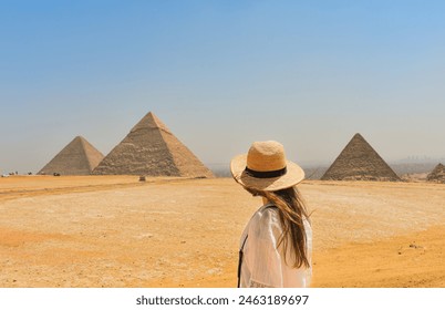 Back view of a woman wearing a hat, looking at the 3 great pyramids in Egypt