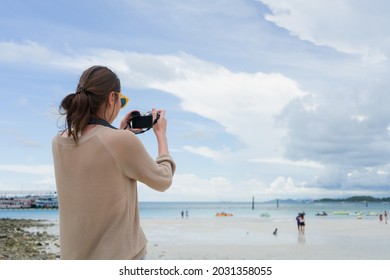 Back View Of Woman Wearing Sunglasses Standing On The Beach Take A Photo By Digital Camera With Sunny Day