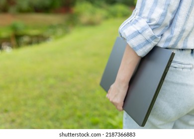 Back View Of A Woman Who Is Standing With A Closed Laptop. Rear View People Collection. Backside View Of Person. Young Engineer With A Closed Laptop In Hand.