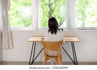 Back view of woman working on laptop at window table