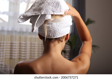 Back View Of A Woman Wrapped In A Towel Standing Next To The Window, Drying Her Hair After A Morning Shower. Hair Care Concept