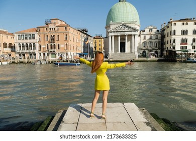 Back View Of Woman In Yellow Clothes Standing With Outstretched Hands On Pier Of Venetian Grand Canal