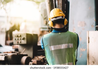 Back view of Work at factory.Asian worker man  working in safety work wear with yellow helmet l ear muff.machanic male in factory workshop industry machine professional