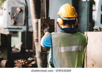 Back View Of Work At Factory.Asian Worker Man  Working In Safety Work Wear With Yellow Helmet L Ear Muff.machanic Male Asia In Factory Workshop Industry Machine Professional