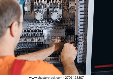 Back view worker technician adjusting industrial control panel in factory.