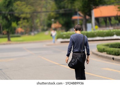 Back view of a working man with a long dark shirt and carry a bag in the park.
