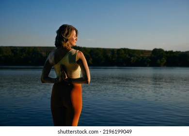 Back view of yogi woman holding hands in namaste pose and meditating on the dock near the lake. - Powered by Shutterstock