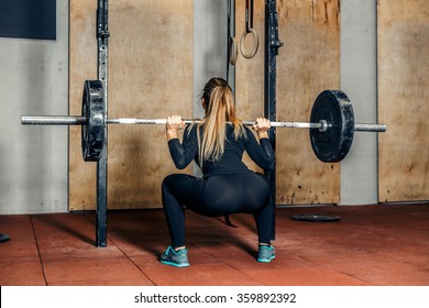 Back view young adult girl doing heavy duty squat in gym with barbell. Woman with perfect abs doing squat exercises. Blonde fit woman in great shape. Fitness