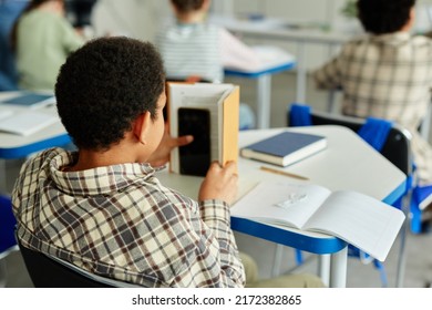 Back View At Young African American Kid Hiding Smartphone In Book And Cheating In Class