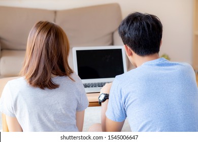 Back View Of Young Asian Couple Working Laptop With Blank Screen Display, Family Planning And Searching Content Together, Man And Woman Looking Computer, Business And Communication Concept.