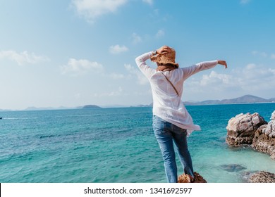 Back view of young asian woman looking from cliff. Future and research concept. Woman with hands up standing on cliff over sea. Travel concept, concepts of winner, freedom, 
