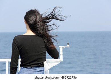 Back view of young asian woman with waving long hair looking at the sea from the deck of cruise ship