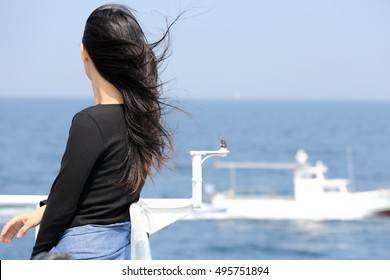 Back view of young asian woman with waving long hair from the deck of cruise ship