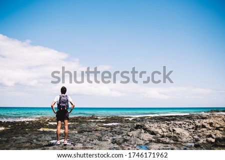 Back view of young backpacker adoring beauty of nature landscape at Menorca coastline, male tourist with travel rucksack spending summer vacations for visiting paradise environment for recreate