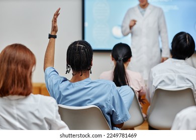 Back view at young black doctor raising hand in audience at medical seminar, copy space