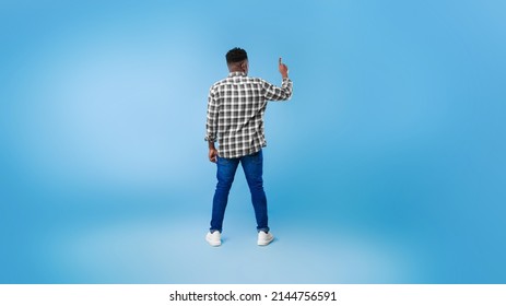 Back view of young black guy pushing button on virtual screen over blue studio background, mockup for design. Millennial African American man interacting with touchscreen, panorama - Shutterstock ID 2144756591