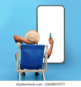 Back view of young black guy sitting in lounge chair with bottle of beer, sipping alcoholic beverage, looking at phone with blank screen on blue studio background, mockup for travelling offer, collage - Powered by Shutterstock