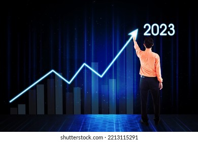 Back View Of Young Businessman Drawing Upward Arrow With 2023 Numbers On The Virtual Screen