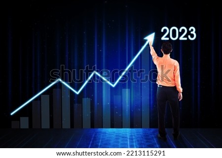 Back view of young businessman drawing upward arrow with 2023 numbers on the virtual screen