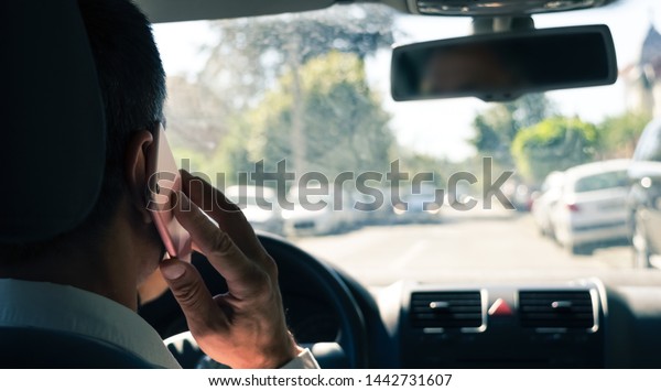 Back view of young businessman driving\
car and talking on mobile phone at the same\
time.