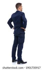 back view of young businessman in navy blue suit holding hands on hips and standing isolated on white background in studio