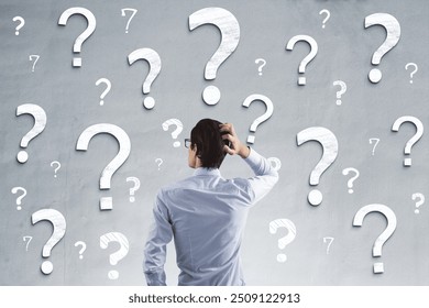 Back view of young businessman on concrete wall background with question marks. Solution and confusion concept - Powered by Shutterstock