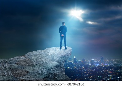 Back View Of Young Businessman On Mountain Top Looking At Night City With Moonlight. Employment Concept. Copy Space