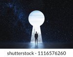 Back view of young businessman standing against keyhole door on starry sky background. Dream, success, opportunity and startup concept