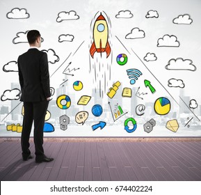 Back view of young businessman standing on wooden deck and looking at abstract business sketch on city background. Marketing concept. Double exposure  - Powered by Shutterstock