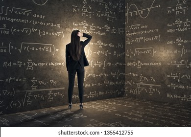 Back view of young businesswoman in concrete corner with mathematical formulas. Complex algorithm and math concept - Shutterstock ID 1355412755