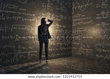 Back view of young businesswoman in concrete corner with mathematical formulas. Complex algorithm and math concept