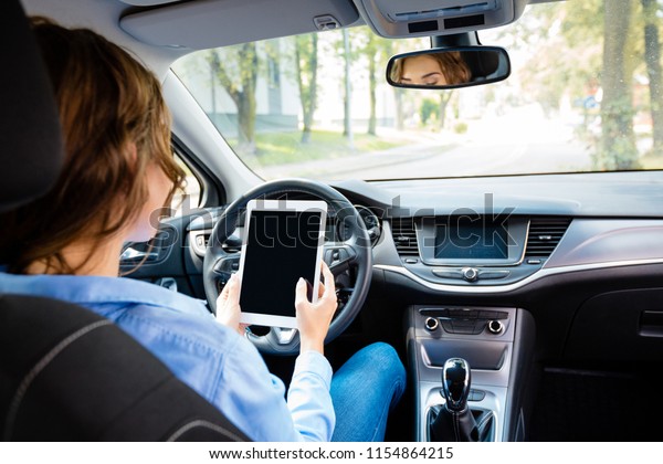 Back view of young businesswoman driving\
driverless car and using digital tablet.\
