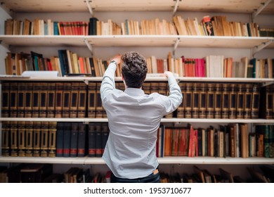 Back view young caucasian man choosing a book from bookshelves - Powered by Shutterstock