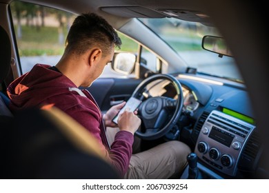 Back View Of Young Caucasian Man Checking Mobile Phone For Messages Or Navigation App For Destination While Sitting In Car Driving Or Parking Real People Travel Concept