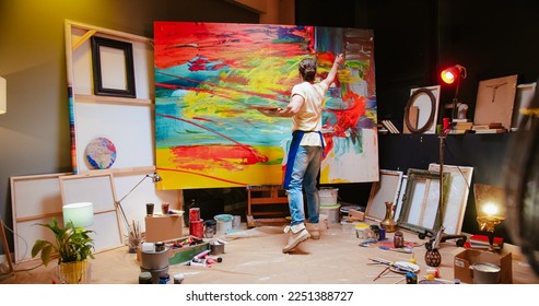 Back view of young Caucasian man painter emotionally drawing on big canvas using paint brush in cozy workshop creating abstract oil painting, contemporary fine art painter, creativity concept - Powered by Shutterstock
