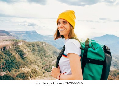 Back view young cheerful girl backpacker with brunette hair relaxation on top rocky mountains, with backpack, yellow hat. Leisure after walking valley, copy space. Looking at camera. - Powered by Shutterstock