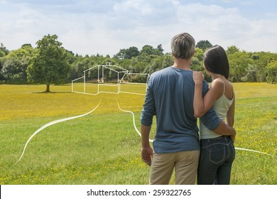 Back View Of A Young Couple Contemplating A Landscape While Imagining Their Future Home, We See A Drawing Of The House On The Countryside With An Imaginary Path