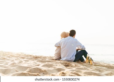 Back View Of A Young Couple Drinking Beer While Sitting On A Beach, Relaxing