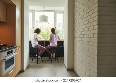 Back View Of Young Couple Eating During Having Breakfast At Table Of Windowsill. Concept Of Domestic Lifestyle. Idea Of Relationship And Spending Time Together. Morning Time. Modern Studio Apartment