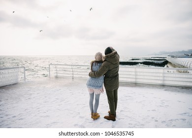 Back View Of Young Couple Embracing On Winter Quay And Looking At The Sea