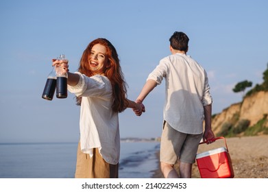 Back View Young Couple Friend Family Man Woman In White Clothes Show Beer Bottle Picnic Bag Refrigerator Hands Walk Rest Together At Sunrise Over Sea Beach Outdoor Seaside In Summer Day Sunset Evening