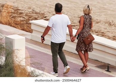 Back view of young couple holding hands while walking on promenade - Powered by Shutterstock