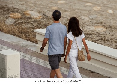 Back view of young couple holding hands while walking on promenade - Powered by Shutterstock